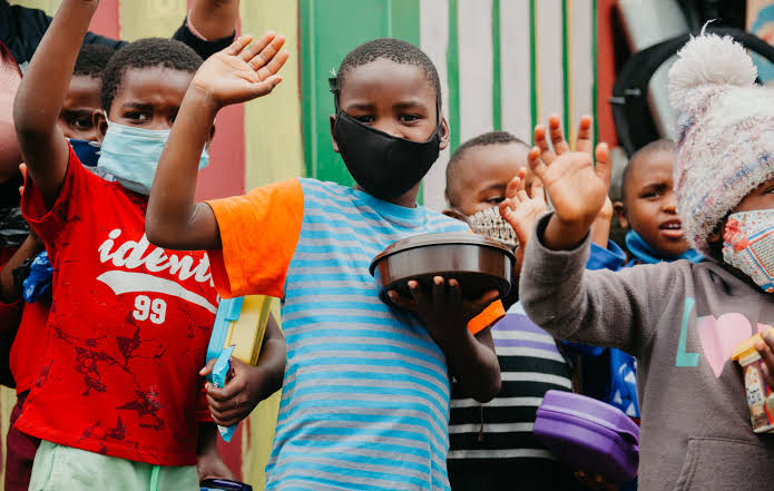 Children waving while holding meals at a township feeding programme
